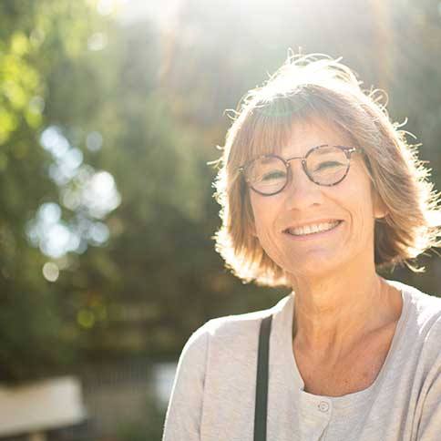 Senior woman with glasses smiling outside on sunny day